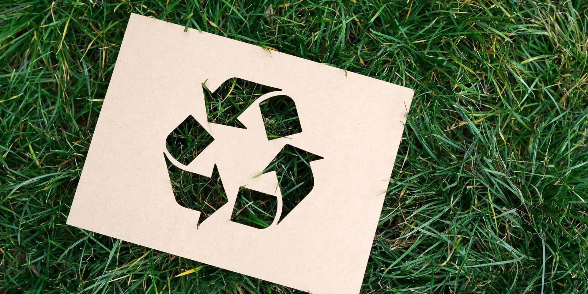 A cardboard cut out of the recycling symbol on grass.