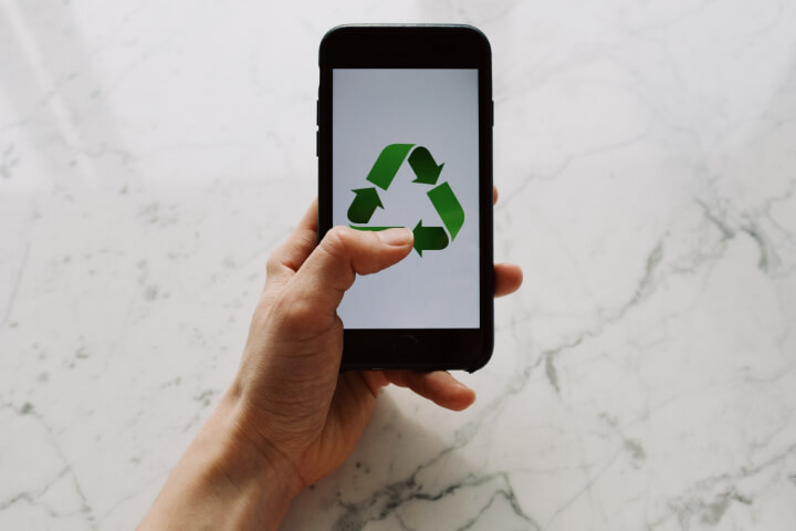 A person holding up a phone with a green recycling symbol on it.