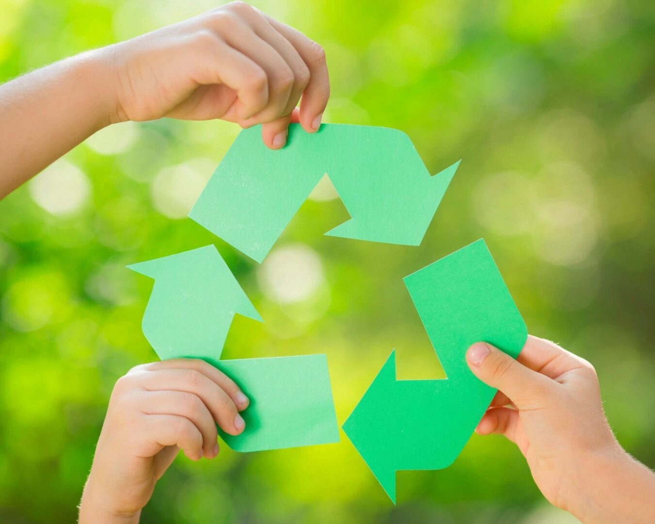 Four hands holding up green paper to recycle symbol.